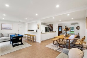 A modern living room with a pool table, a dining area with a wooden table and chairs, a kitchen with white cabinets, and a staircase leading to an upper level. - Genesta Ocean Sands Cowes (Cowes)