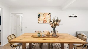 A dining room with a wooden table, chairs, a vase with flowers, and a painting on the wall. - Genesta Ocean Sands Cowes (Cowes)