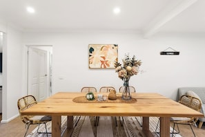A dining room with a wooden table, chairs, a vase with flowers, and a painting on the wall. - Genesta Ocean Sands Cowes (Cowes)