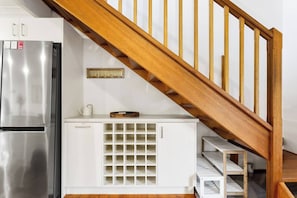 A kitchen with a stainless steel refrigerator, a wooden staircase, and a white cabinet with a grid of shelves. - Genesta Ocean Sands Cowes (Cowes)
