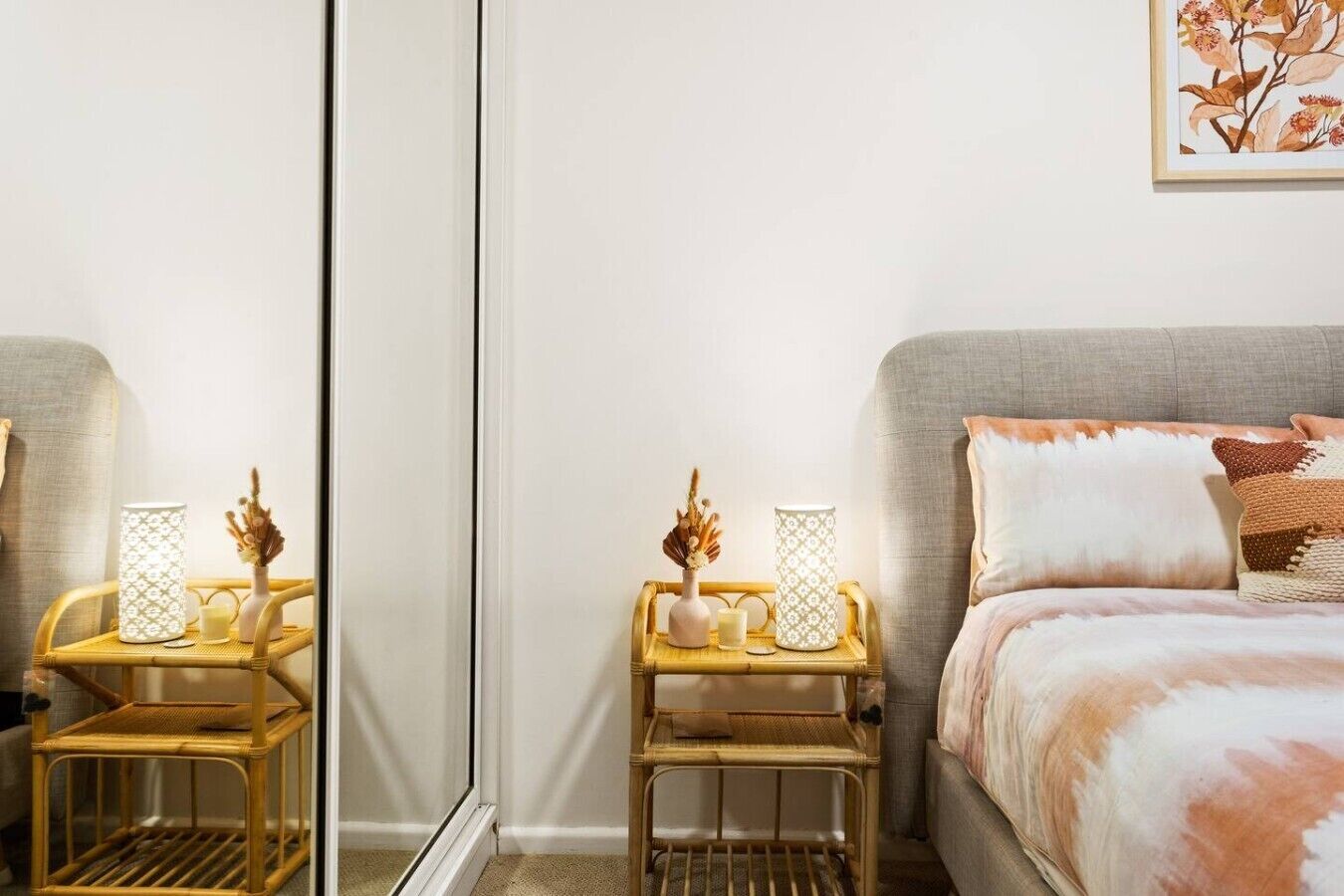A bedroom with a bed, bedside tables, a mirror, and a wall-mounted artwork.