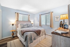 Ein Schlafzimmer mit Bett, Nachttischen, einer Lampe und einem Fenster mit Jalousien.