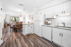 A modern kitchen with white cabinets, a built-in dishwasher, and a dining area with a wooden table and chairs. - Fiddlers Cove Gated Resort- Pools- Hot Tub - Tennis - Pickle Ball walk to Beach! (Hilton Head Island)