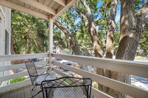 A balcony with a metal chair and table, overlooking a parking area and trees. - Fiddlers Cove Gated Resort- Pools- Hot Tub - Tennis - Pickle Ball walk to Beach! (Hilton Head Island)