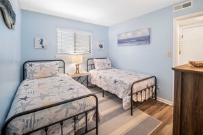 A bedroom with two beds, a window with blinds, a nightstand with a lamp, and a painting on the wall. - Fiddlers Cove Gated Resort- Pools- Hot Tub - Tennis - Pickle Ball walk to Beach! (Hilton Head Island)