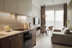A modern kitchen with a built-in oven, a dining area with a sofa and chairs, and a large window with curtains. - Olivia Pulse Gdańsk (Gdańsk)