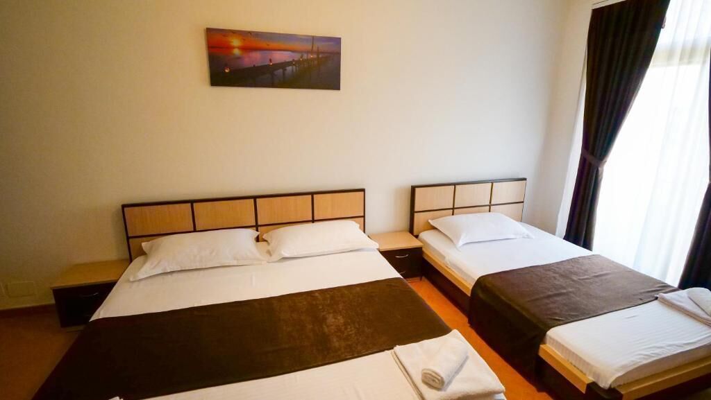 Une chambre d’hôtel avec deux lits, une table de chevet, un tableau au mur et une fenêtre avec des rideaux.
