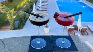 Udsigt over poolen med to drikkevarer på et bord, overblik over pool og anlagt område.