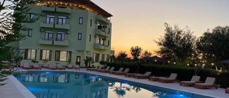 Un hotel con piscina, sillas de descanso y un edificio de varios pisos con balcones.