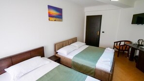 A hotel room with two beds, a desk, a chair, a TV, and a door.