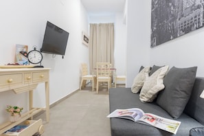 Ein modernes Wohnzimmer mit grauem Sofa, Flachbildfernseher, Holzschreibtisch und Bücherregal.