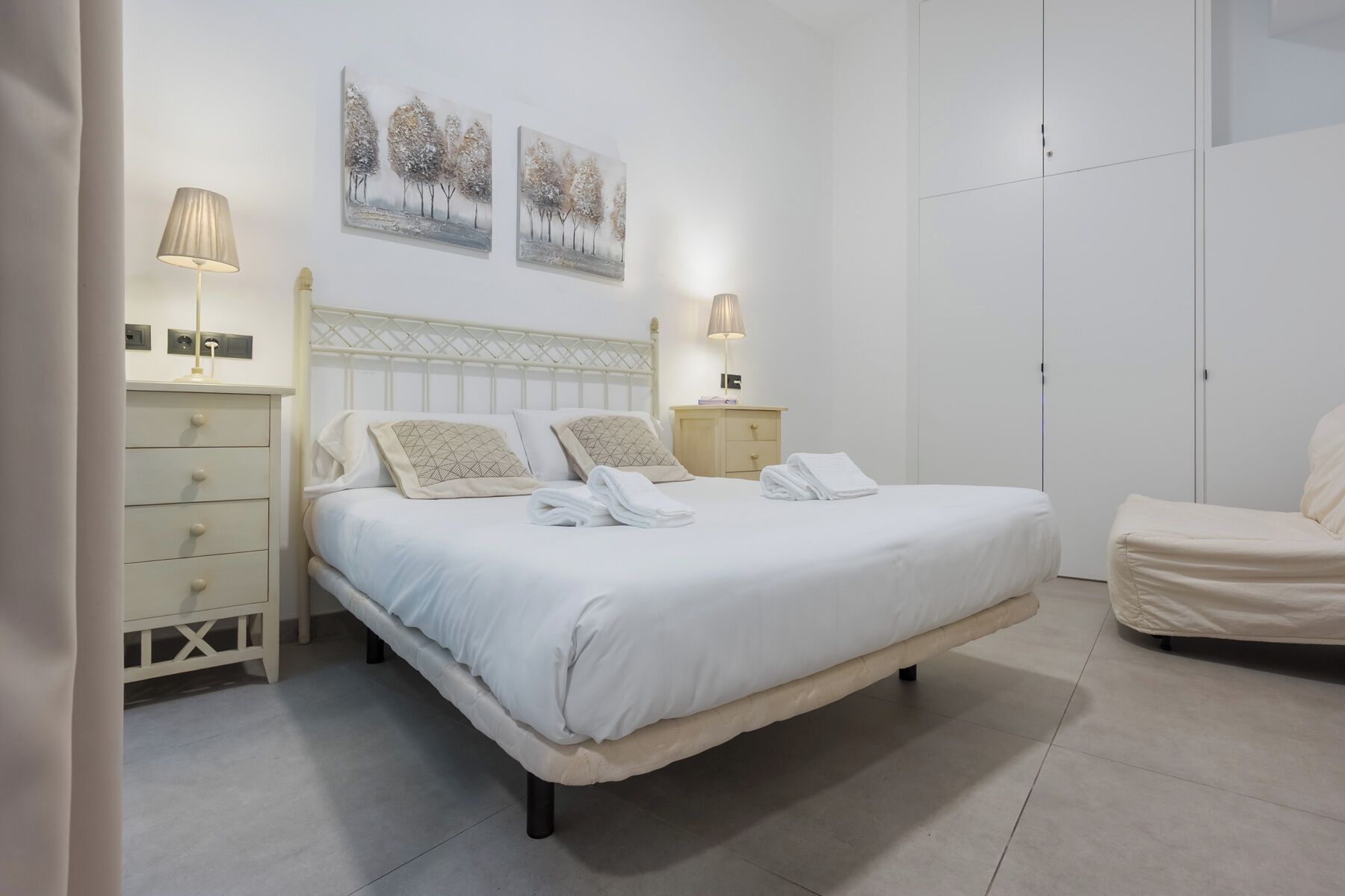 Une chambre à coucher comprenant un lit, deux tables de chevet, une armoire et deux tableaux accrochés au mur.