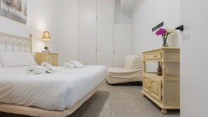 Ein Hotelzimmer mit Bett, Stuhl, Nachttisch, Lampe, Kommode und einer Vase mit Blumen.