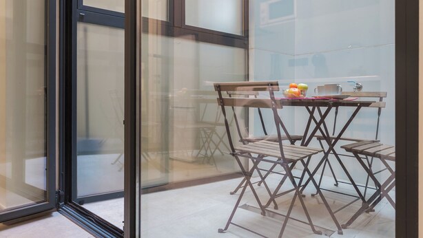 Ein verglaster Balkon mit einem Holztisch und Stühlen, einer Obstschale und einer Tasse.