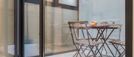 A glass-enclosed balcony with a wooden table and chairs, a bowl of fruit, and a cup.