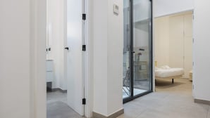 Ein Hotelgang mit einer Glastür, die zu einem Zimmer mit einem Bett und einem kleinen Tisch führt.