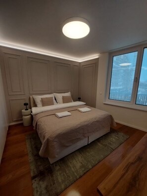 A bedroom with a bed, a bedside table, a nightstand, a window, and a ceiling light. - The Royal Suite under the castle with river views & private parking (Bratislava-Staré Mesto)