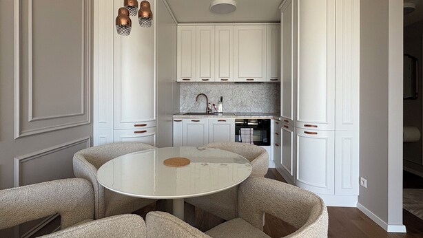A compact kitchen with white cabinetry, a round dining table, and a built-in oven. - The Royal Suite under the castle with river views & private parking (Bratislava-Staré Mesto)