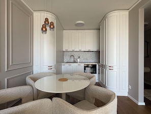 A compact kitchen with white cabinetry, a round dining table, and a built-in oven. - The Royal Suite under the castle with river views & private parking (Bratislava-Staré Mesto)