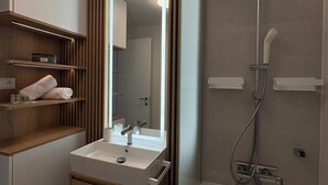 A modern bathroom with a built-in sink, mirror, wooden vanity, and a shower with a handheld showerhead. - The Royal Suite under the castle with river views & private parking (Bratislava-Staré Mesto)