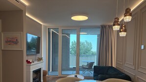 A modern living room with a fireplace, a round table with chairs, a television mounted on the wall, and a balcony with outdoor furniture. - The Royal Suite under the castle with river views & private parking (Bratislava-Staré Mesto)