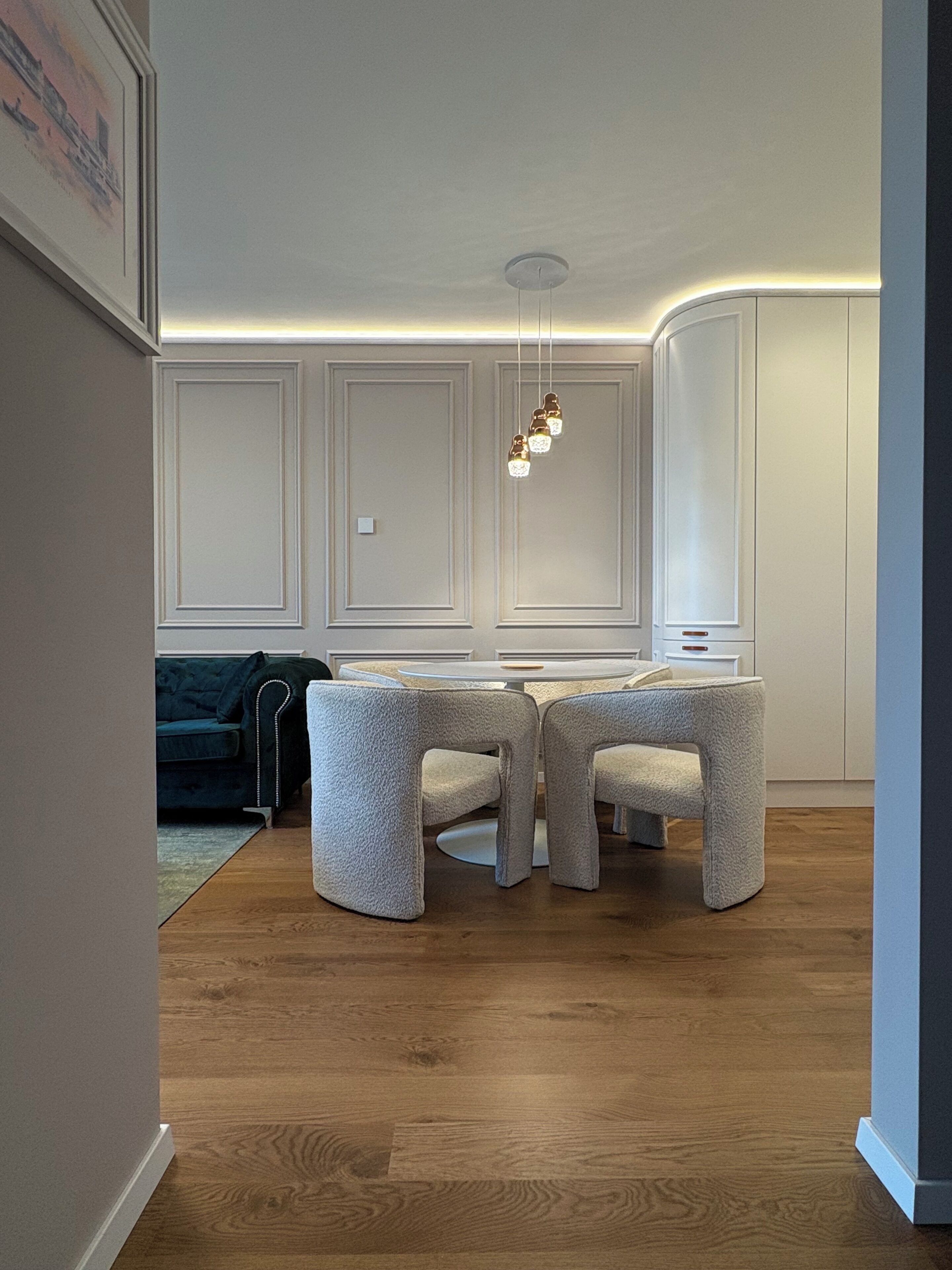 Ein moderner Essbereich mit einem runden Tisch, vier Stühlen, einer Hängeleuchte und einer dunkelgrauen Couch im Hintergrund.