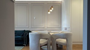 Ein moderner Essbereich mit einem runden Tisch, vier Stühlen, einer Hängeleuchte und einer dunkelgrauen Couch im Hintergrund.