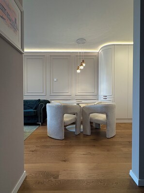 A modern dining area with a round table and four chairs, a hanging light fixture, and a dark-colored sofa in the background. - The Royal Suite under the castle with river views & private parking (Bratislava-Staré Mesto)