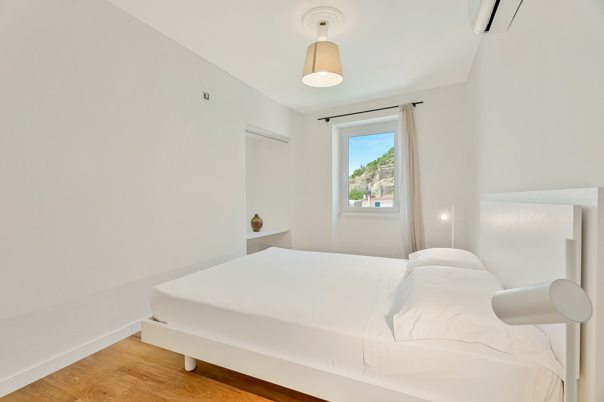 A bedroom with a bed, a window, a ceiling light, and a wall-mounted air conditioner.