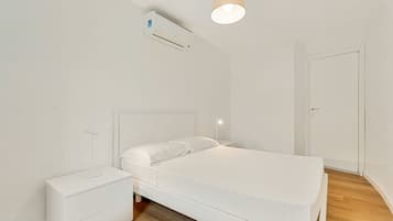 A minimalist bedroom with a bed, bedside table, nightstand, and an air conditioning unit.