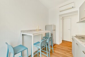 A compact kitchen with a white countertop, a refrigerator, and two blue chairs.