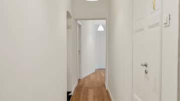 A hallway with wooden flooring, white walls, and doors with a number plate.