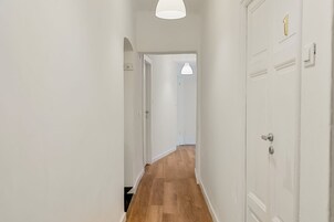 Un pasillo con piso de madera, paredes blancas y puertas con placa de número.