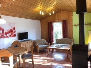 A cozy cabin interior with wooden walls, a TV, two sofas, a dining table, and a wood stove. - Komfortabler Doppelbungalow mit Terrasse im Ferienpark Mirow (Mirow)