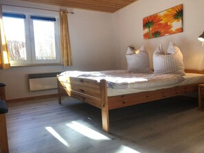 A room with a wooden bed, a window with curtains, a radiator, and a wall-mounted lamp. - Komfortabler Doppelbungalow mit Terrasse im Ferienpark Mirow (Mirow)