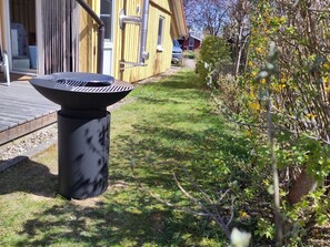 Une terrasse avec un barbecue, une plateforme en bois et un espace jardin agrémenté d’arbustes et d’un arbre.