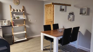 A dining area with a wooden table and black chairs, a white shelf with decorative items, and a wooden door. - Moderner Doppelbungalow mit Terrasse im Ferienpark Mirow (Mirow)