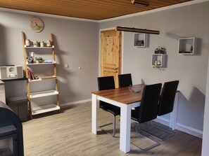 Ein Essbereich mit Holztisch und schwarzen Stühlen, einem weißen Regal mit Dekoration und einer Holztür.