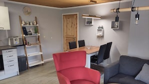 A modern living room with a red armchair, a gray sofa, a wooden dining table, and a small coffee table. - Moderner Doppelbungalow mit Terrasse im Ferienpark Mirow (Mirow)