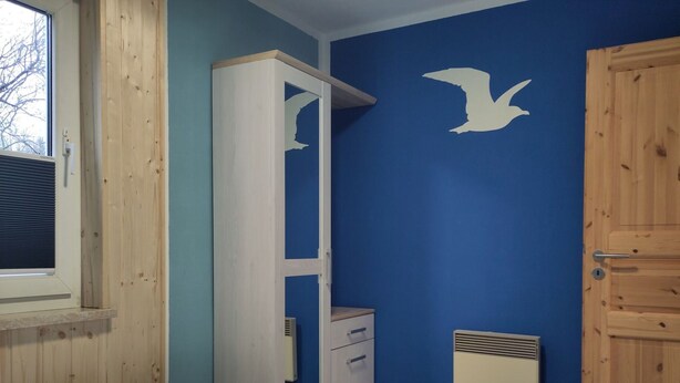 A bedroom with two beds, a wardrobe, a radiator, and a wall with a bird decal. - Moderner Doppelbungalow mit Terrasse im Ferienpark Mirow (Mirow)