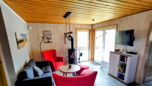 A living room with a black sofa, red chairs, a small round table, a television, and a fireplace. - Moderner Doppelbungalow mit Terrasse im Ferienpark Mirow (Mirow)
