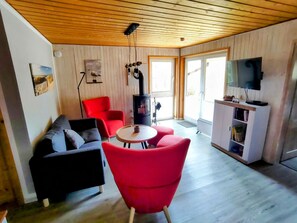 Ein Wohnzimmer mit einer schwarzen Couch, roten Sesseln, einem kleinen runden Tisch, einem Fernseher und einem Kamin.