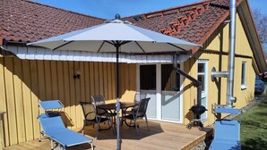 A wooden deck with a table and chairs, a barbecue grill, and a covered seating area with an umbrella. - Moderner Doppelbungalow mit Terrasse im Ferienpark Mirow (Mirow)
