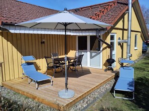 A wooden deck with a table and chairs, a barbecue grill, and a covered seating area with an umbrella.