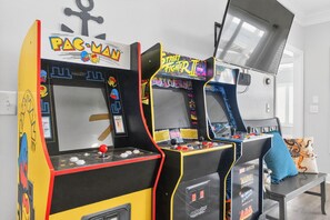Two arcade machines with Pac-Man and Street Fighter II labels, a bench, and a window with a view. - Endless Summer, Oceanfront, 8 Bdrm, Pvt. Htd Pool, Pvt. Direct Beach Access (Holden Beach)