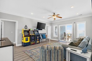 A living room with a ceiling fan, a flat-screen TV, and a gaming console. - Endless Summer, Oceanfront, 8 Bdrm, Pvt. Htd Pool, Pvt. Direct Beach Access (Holden Beach)