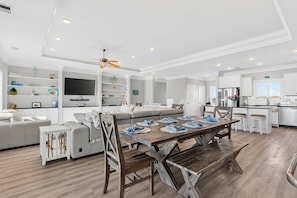 A spacious living area with a large dining table, a sofa, and a television mounted on the wall. - Endless Summer, Oceanfront, 8 Bdrm, Pvt. Htd Pool, Pvt. Direct Beach Access (Holden Beach)