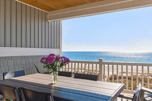 Ein überdachter Außenbereich mit Tisch und Stühlen, mit Blick auf einen Strand.