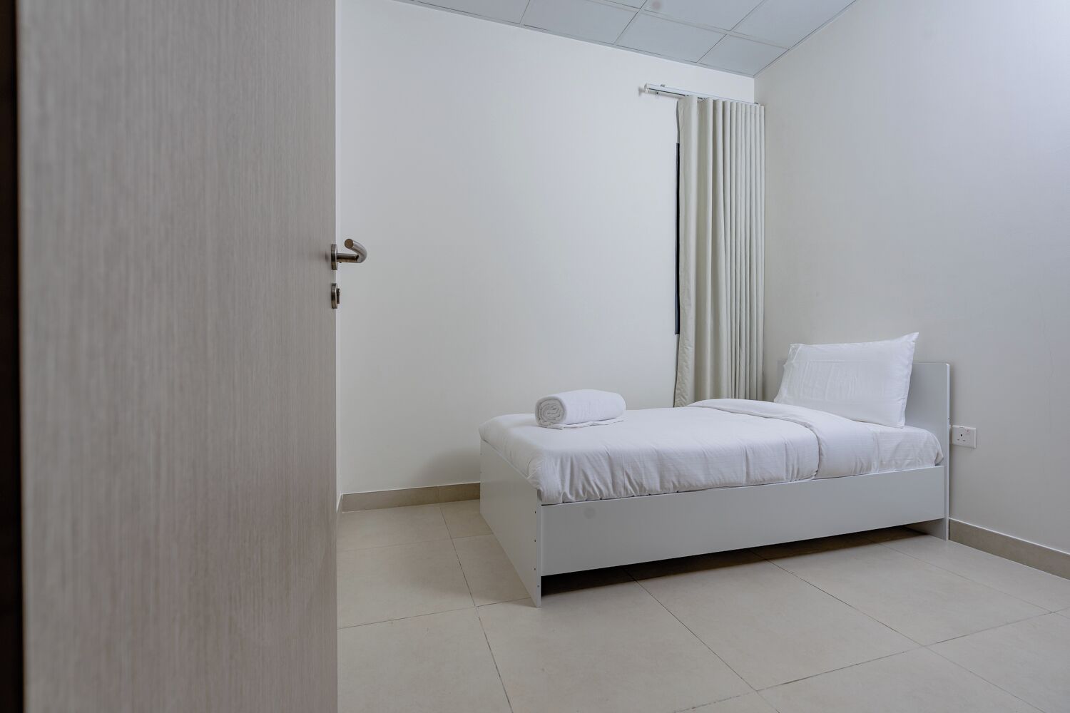A minimalist bedroom with a bed, a door, and a curtain.