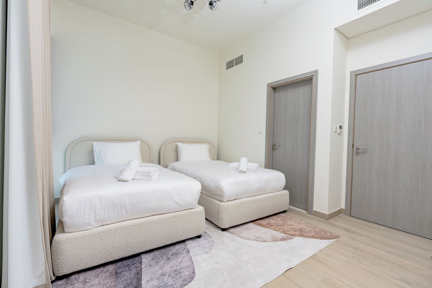 A hotel room with two beds, a door, and a light-colored rug.